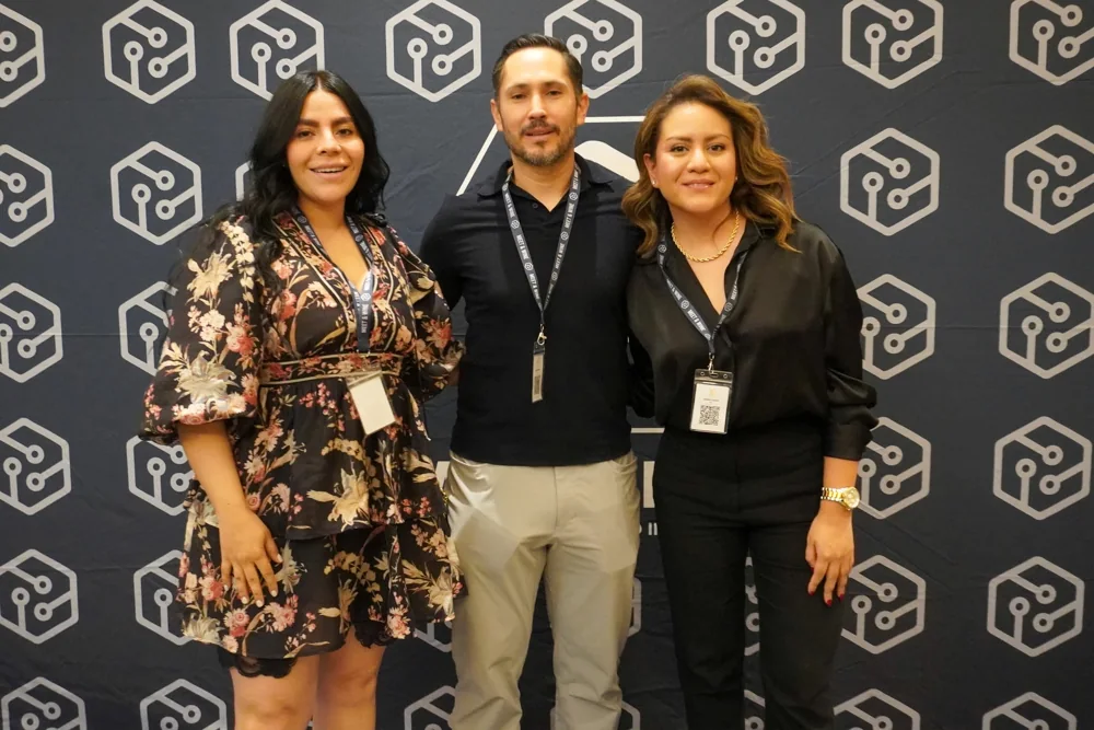 Tres asistentes de un evento frente al fondo institucional de Mekanexia